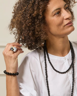 Person wearing a white shirt, black beaded necklace, and a black marble ring with a neutral background