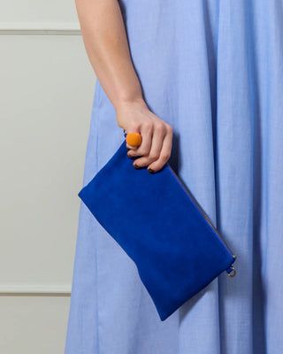 Person holding a blue clutch wearing a bright orange chunky ring with a neutral background