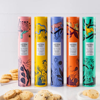 Five colourful cylindrical tins of Shortbread House shortbread on a white background with shortbread rounds around