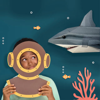 Child with paper cut out of a diver mask beside a 3d paper shark