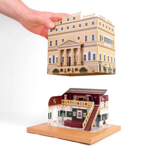 Hand holding a miniature model of a stately home against a white background