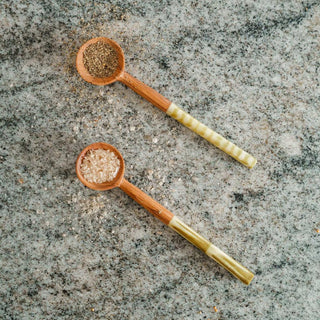 Two wooden spoons with olive green handles on a gray stone surface, filled with spices.