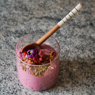 Pink dessert in a glass with a wooden spoon with white handle on a gray stone surface