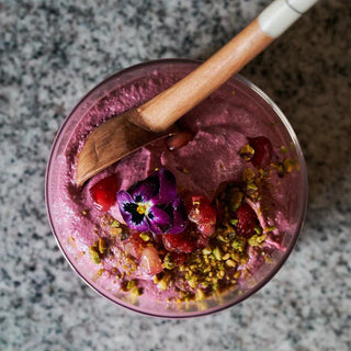 Pink smoothie with garnishes scooped by a wooden spoon with white handle  on a gray surface