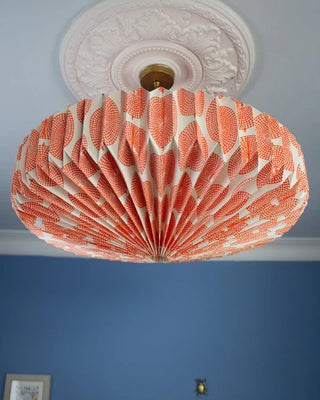Decorative ceiling light shade with an orange and white pattern against a blue wall.