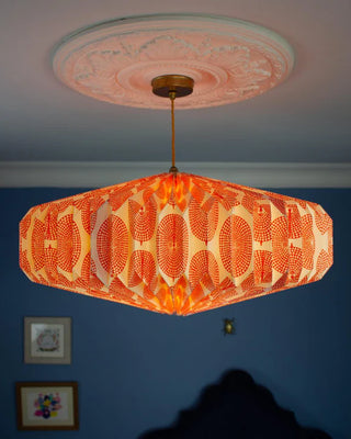 Decorative orange and white origami lampshade hanging from a ceiling with the bulb switched on in a room with blue walls.