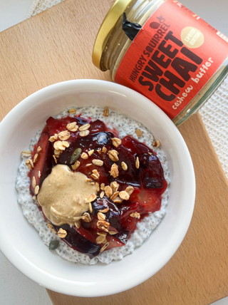 Chia pudding with fruit and nuts in a white bowl next to a jar of sweet chai cashew butter.