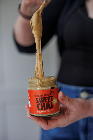 Person holding a jar of 'Sweet Chai' cashew butter with a spoonful being lifted.