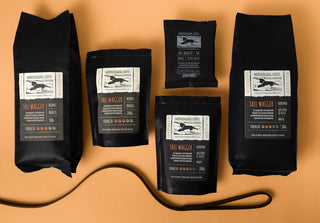 Five black coffee bags with visible branding on a beige background
