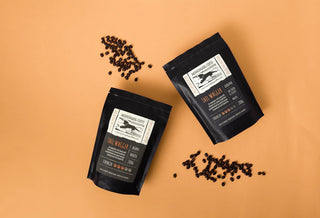 Two black coffee bags with labels on a beige background