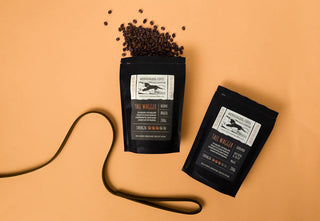 Two black coffee bags with labels, one spilling coffee beans on a beige background