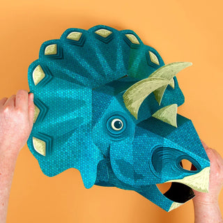 Blue 3d paper triceratops mask with hands against an orange background