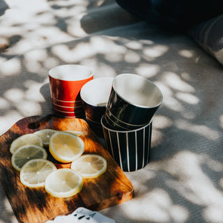 Stacked ceramic cups next to a wooden cutting board with lemon slices, against a textured fabric.