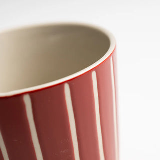 Close-up of a red ceramic mug with white stripes on a light gray background