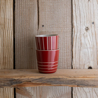 Two red ceramic cups stacked on a wooden surface with a rustic wooden background