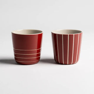 Two red ceramic cups with white interior on a light gray background