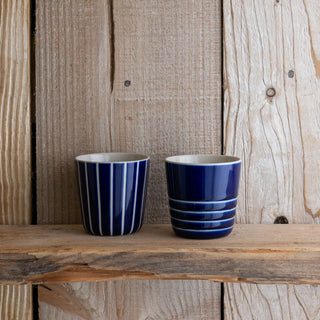 Two blue striped ceramic cups on a wooden surface with a wooden background