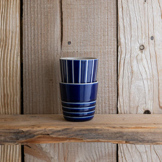 Two blue ceramic cups stacked on a wooden surface with a wooden panel background