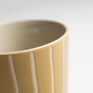Close-up of a yellow ceramic mug with vertical stripes on a light background