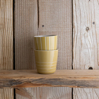 Two yellow ceramic beaker mugs stacked on a wooden surface with a wooden background