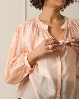 Person wearing a light pink blouse with puffed sleeves against a neutral background wearing nude coloured ring