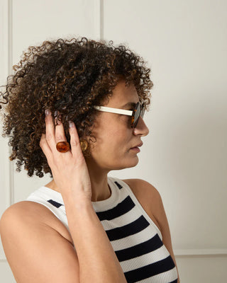 Woman wearing sunglasses and a striped sleeveless top, holding her hand to her ear wearing tortoiseshell ring