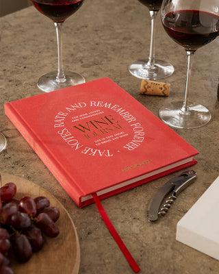 Red wine tasting notebook with wine-themed text on a table with wine glasses and grapes