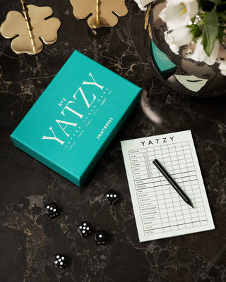 Yatzy box and contents including dice, pencils and scorecard against a dark marble surface