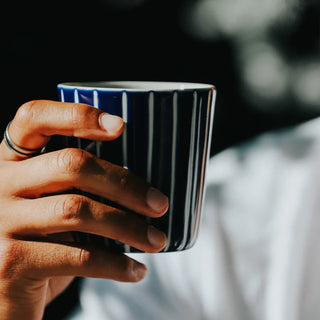 Hand holding a striped mug with a blurred background