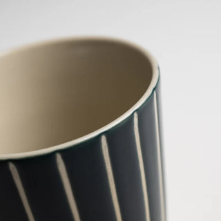 Close-up of a ceramic mug with green and white vertical striped body on a white background