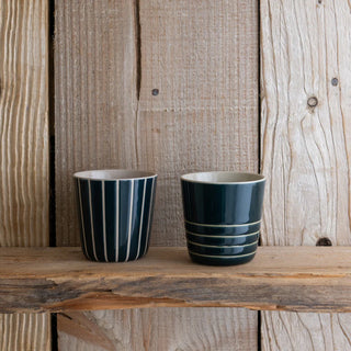 Two green striped ceramic cups on a wooden surface with a rustic wooden background