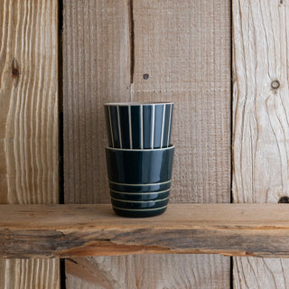 Two dark green striped ceramic cups stacked on a wooden surface with a wooden background